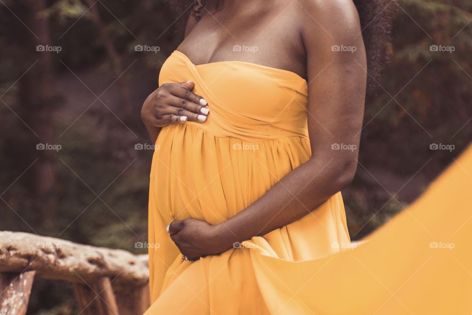 An African American woman holds her pregnant belly in a beautiful yellow dress to celebrate her maternity & motherhood