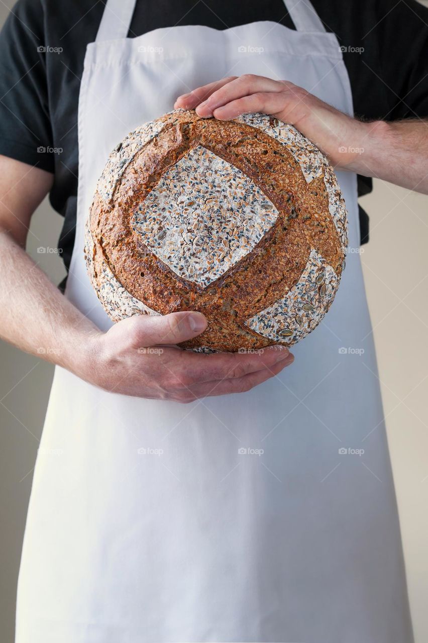 Close-up at bakers hands holding a loaf of sourdough bread in front of him.