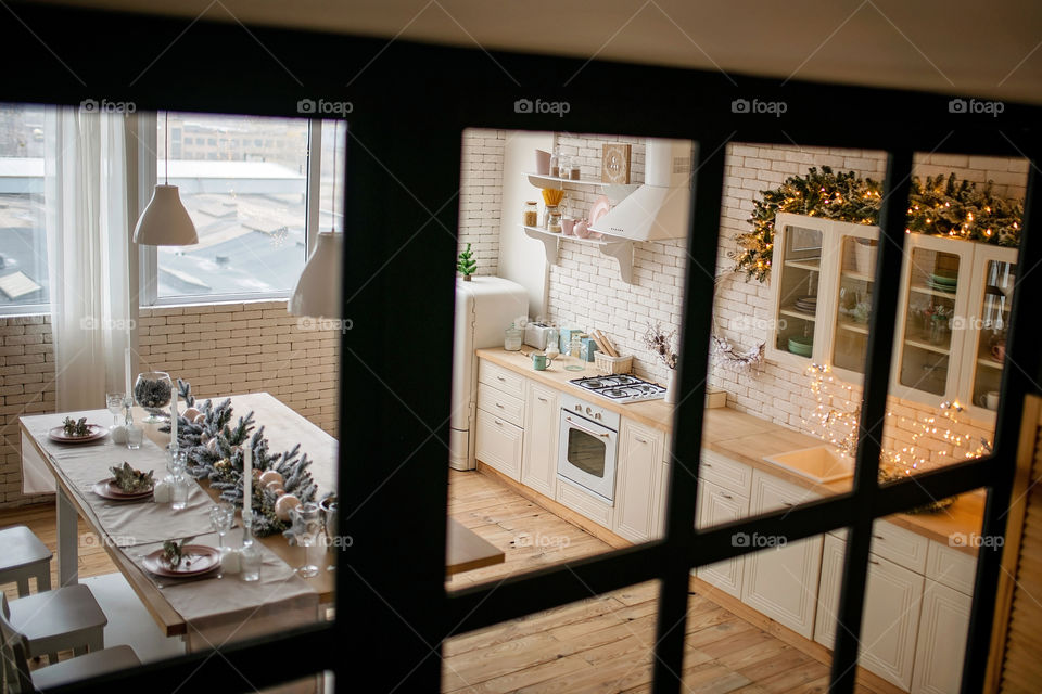 Festive winter cozy kitchen interior with garlands, decorations and gifts.  Christmas dinner at the decorated table.