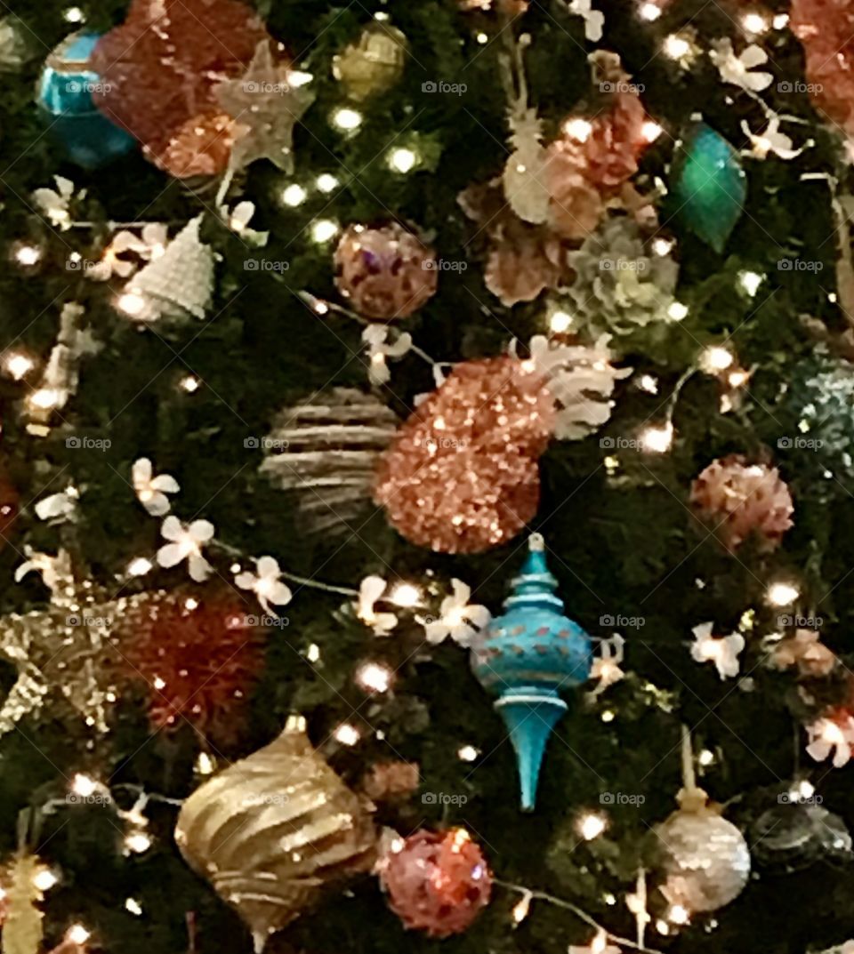 A closeup view of blue, gold, and coral Christmas ornaments on a green Christmas tree with clear lights