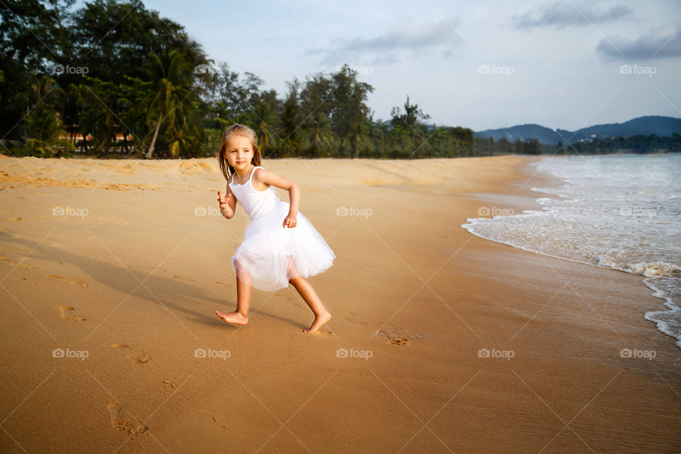 Little girl with blonde hair running on the beach 