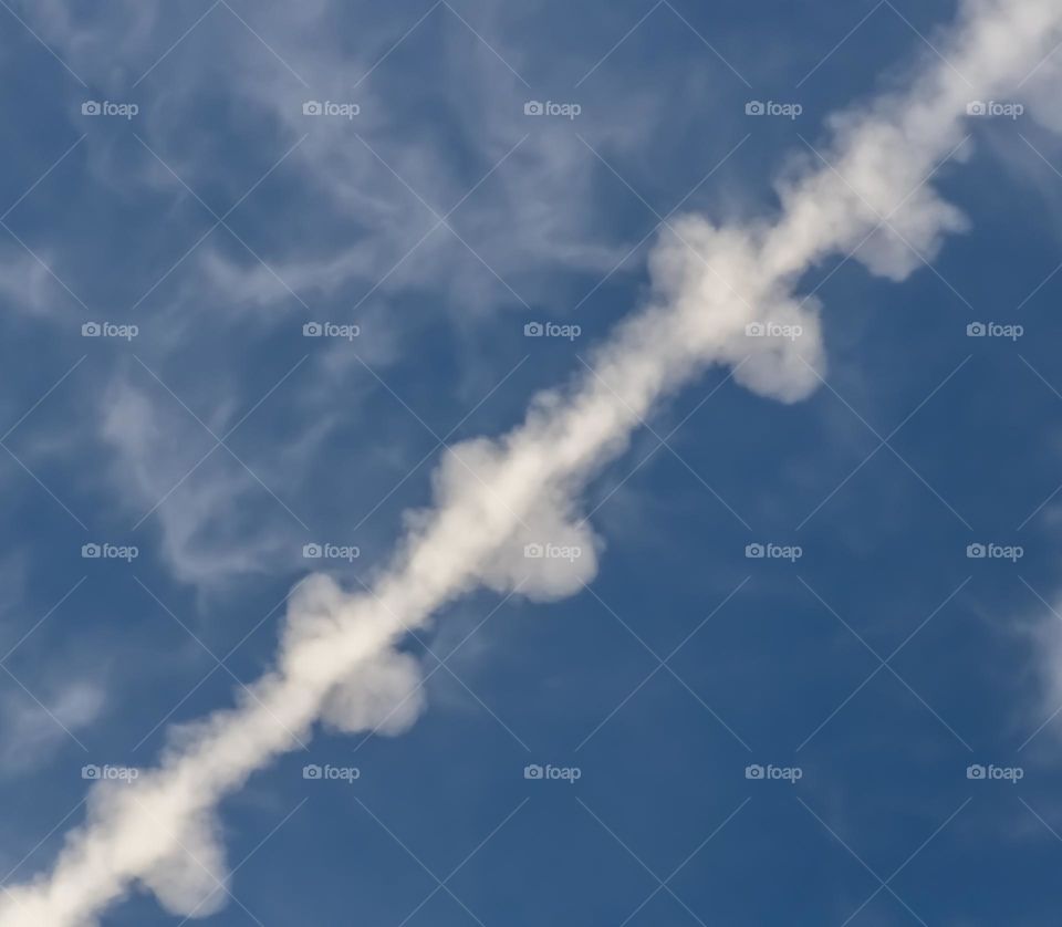 Remnants of vapour trails streak diagonally across a lightly clouded blue sky