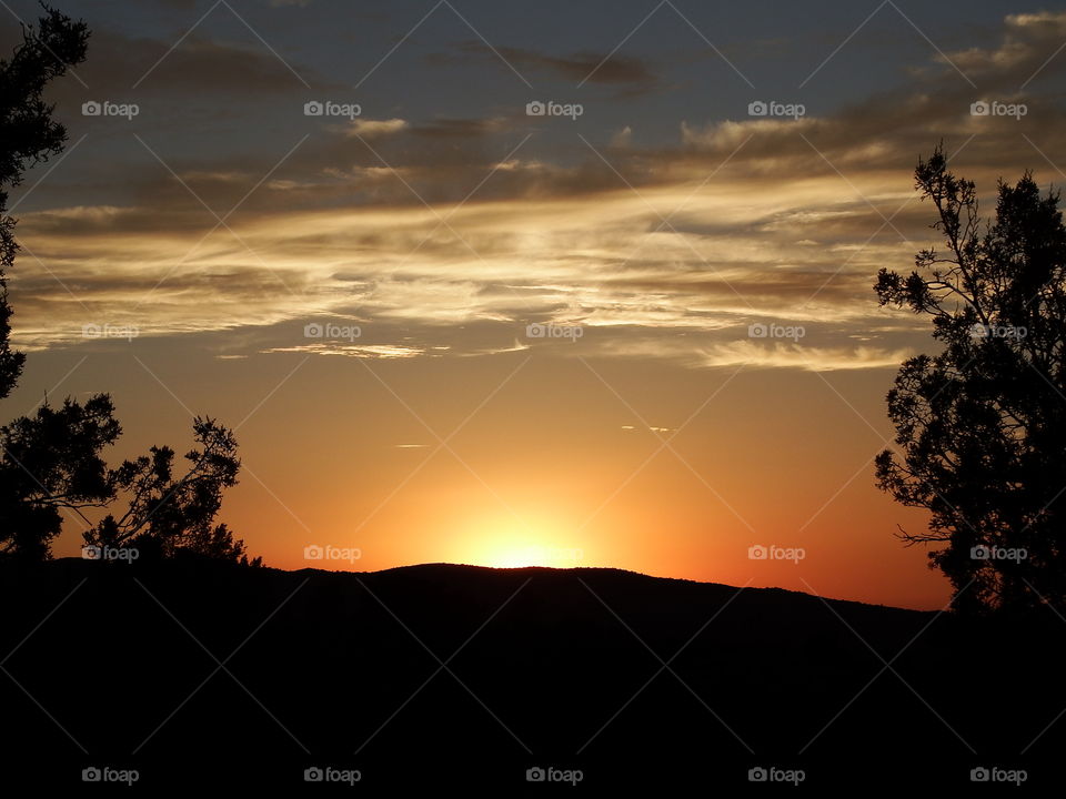 Cloudscape above a golden sunset with silhouetted landscape.