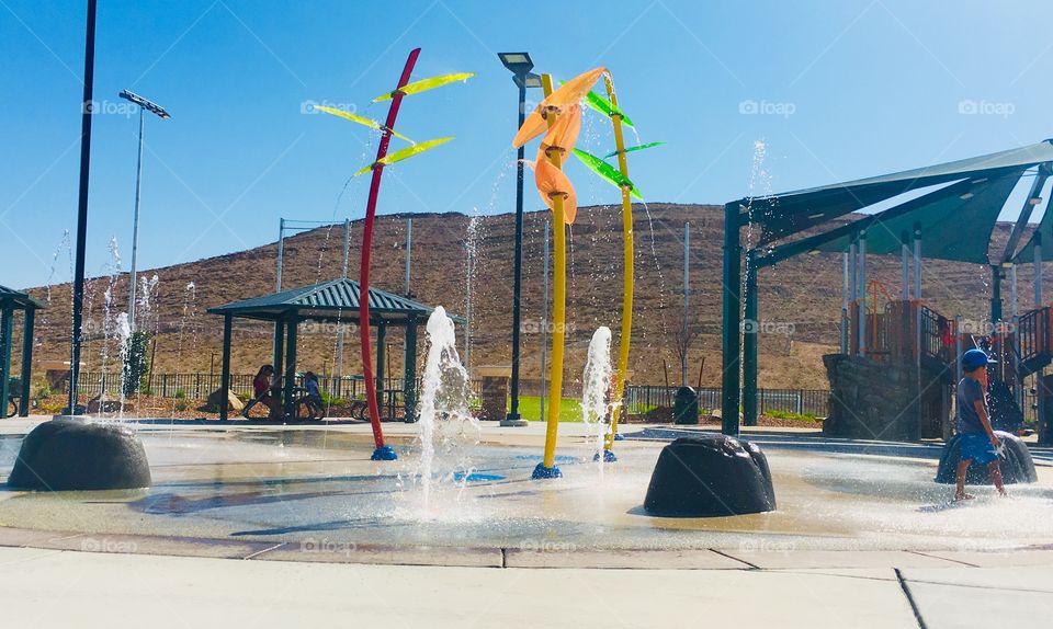 A colorful splash pad in the desert during summertime. Mountain in background, water spraying.