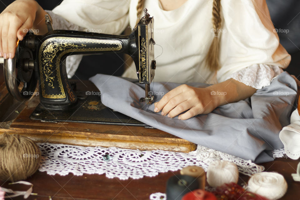 The girl sews on an old sewing machine, beside lie the sewing possessions