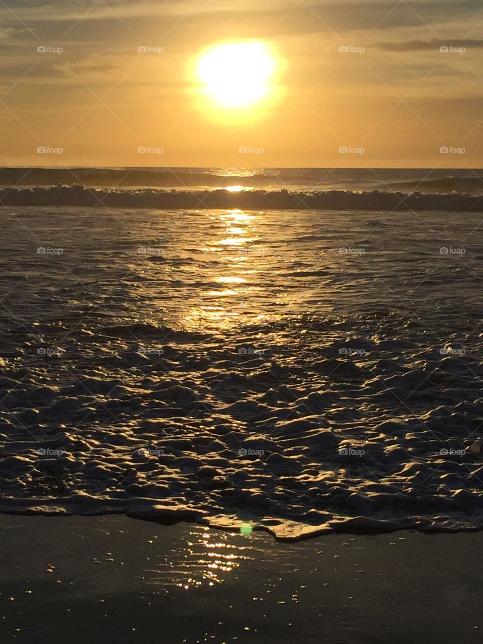 A golden sunset on a San Diego beach.  The waves splash as the light glimmers on the water