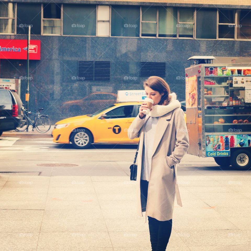 Girl with coffee in New York with a yellow taxi cab driving past. 