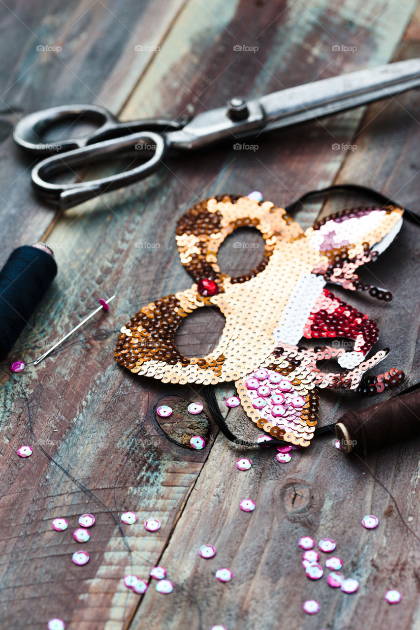 Decorating Christmas reindeer mask with sequins using thread needle and scissors following diy ideas on wooden table