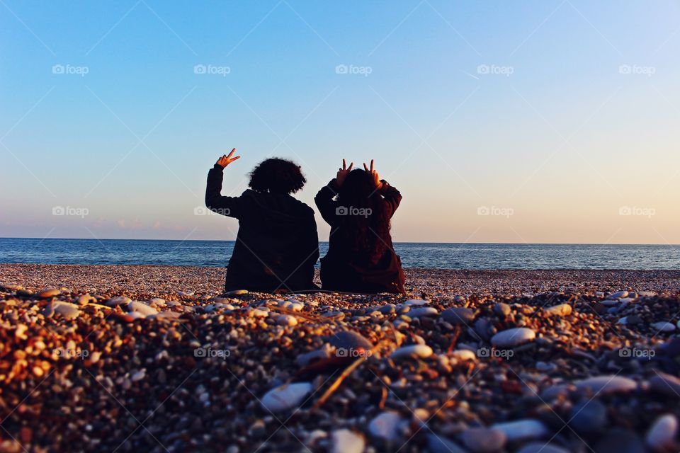 Rear view of two girls making hand sign