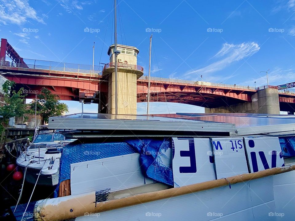 This is the „Pulaski Bridge“ at „Newtown Creek“ in LIC, Queens seen looking over the back of our boat, the „Salvation“ into the sunshine as the sun begins to set behind the horizon. 2023. Hypnotic Productions