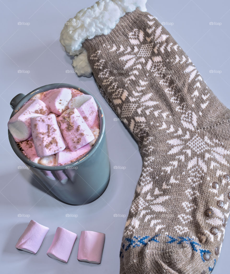 Hot chocolate with marshmallows and chunky, woollen socks on grey background 