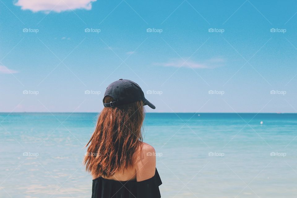 Girl with hat on facing the ocean