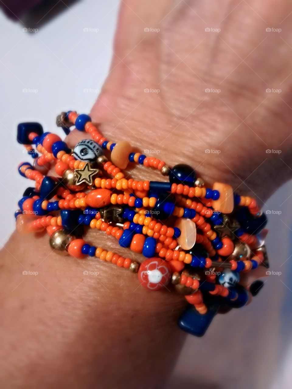 Multi-strand seed bead bracelet accented with blue evil eyes, orange chips and gold stars and balls.