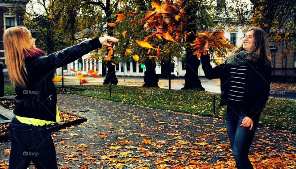 Two young girls playing with autumn leaves
