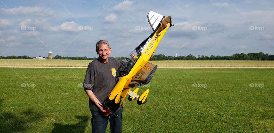 A man is seen in a field holding a remote controlled airplane