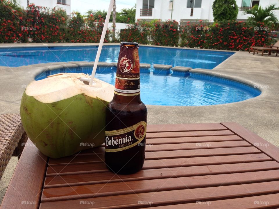 Beer and coconut next to swimming pool. 