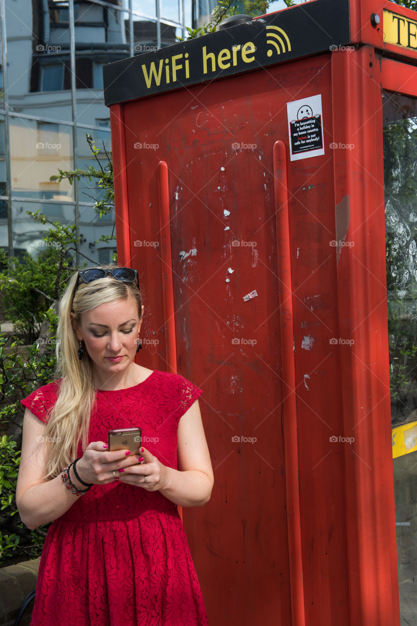 Woman 30 years old looking at her phone and social media at at WiFi spot at a telephone booth in London near Euston Square.