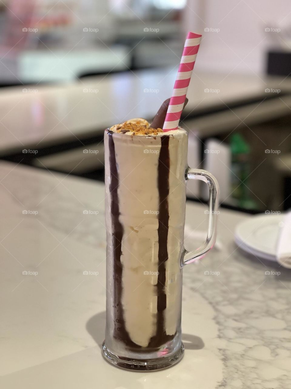 A chocolatey milkshake is ready to consumed at a candy bar. The tall drink includes a candy-striped straw to make it even more fun to drink.