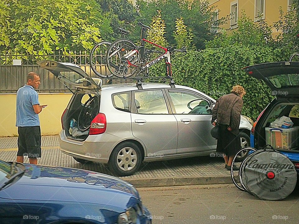 A man watching an old woman who is trying to pass between two cars.