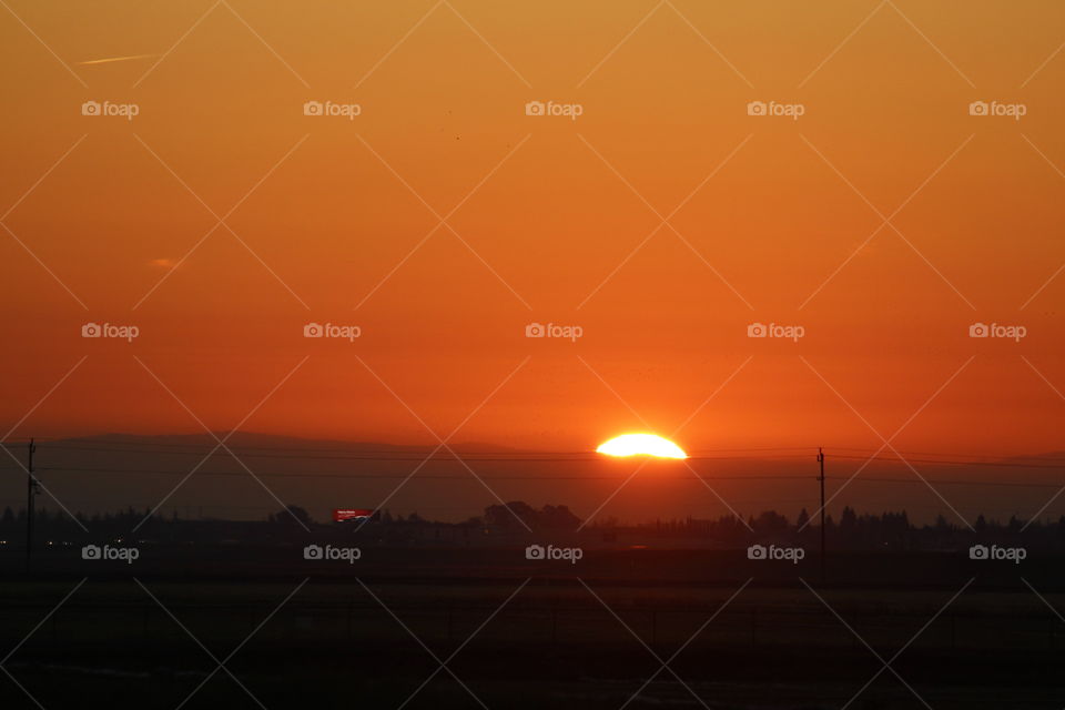 Sunrise, peeking its sun rays over the valley of Sacramento California turning the sky clouds red orange and yellow