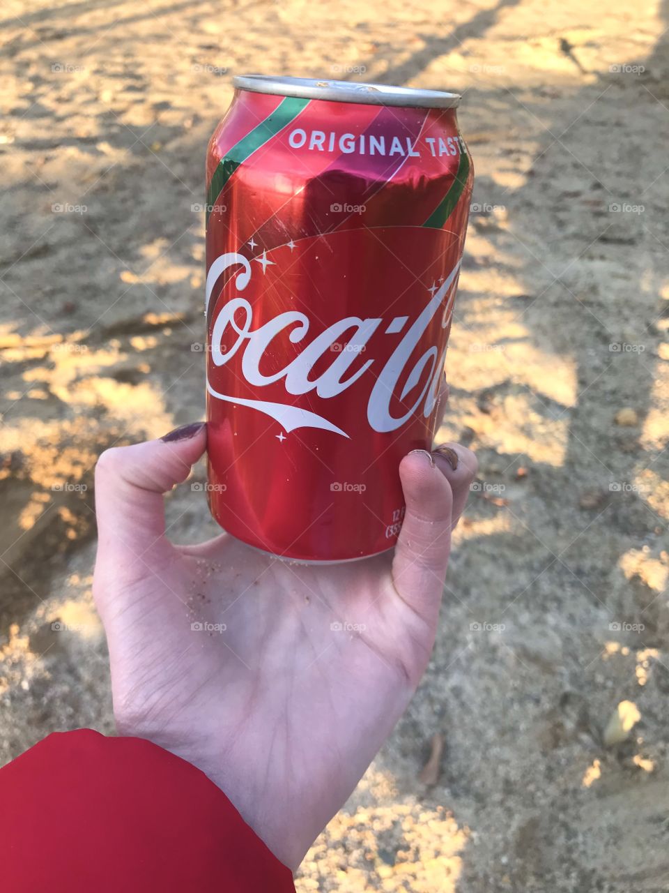 Holding a can of coke by the sand 