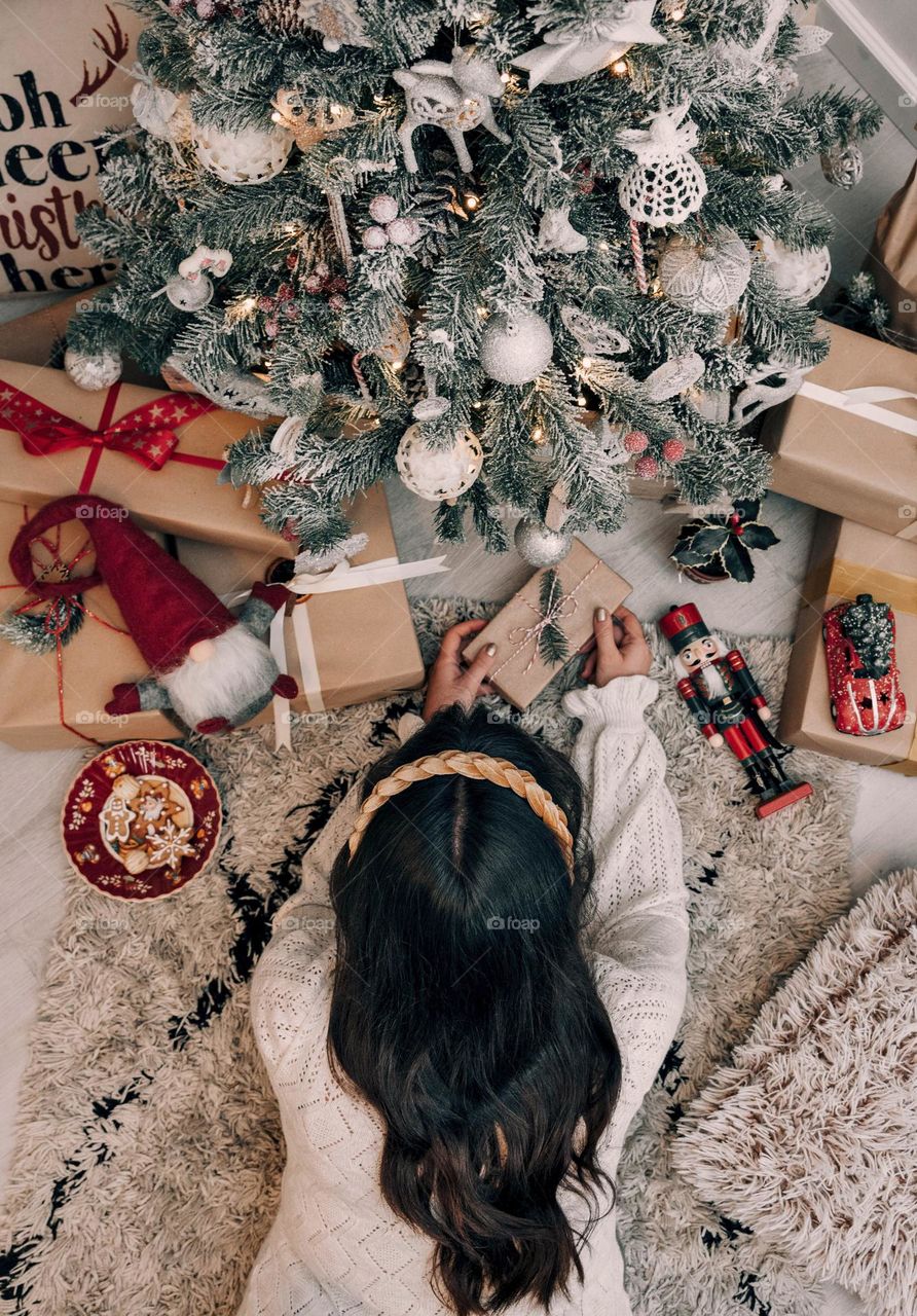 Vertical shot of a woman putting a brown gift box under a Christmas tree