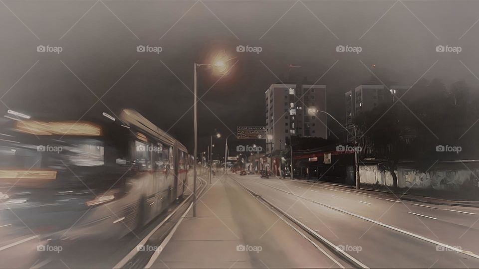 A night cityscape featuring a blurred bus in motion, illuminated by warm streetlights and surrounded by tall buildings. The scene captures the quiet, almost nostalgic atmosphere of urban life at night, with a balance of stillness and movement.