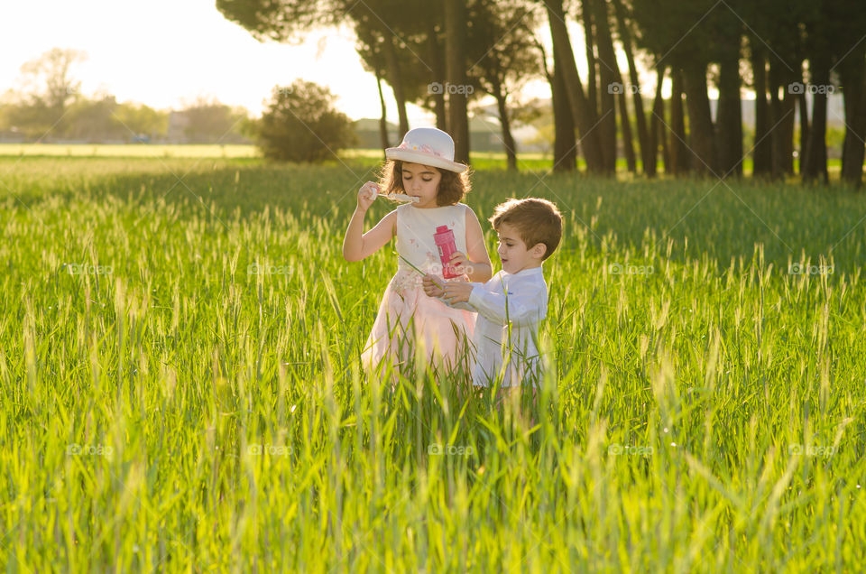 Girl with her brother blowing soap bubble in grassy field