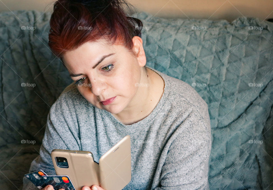 Red haired woman holding credit cards and phone