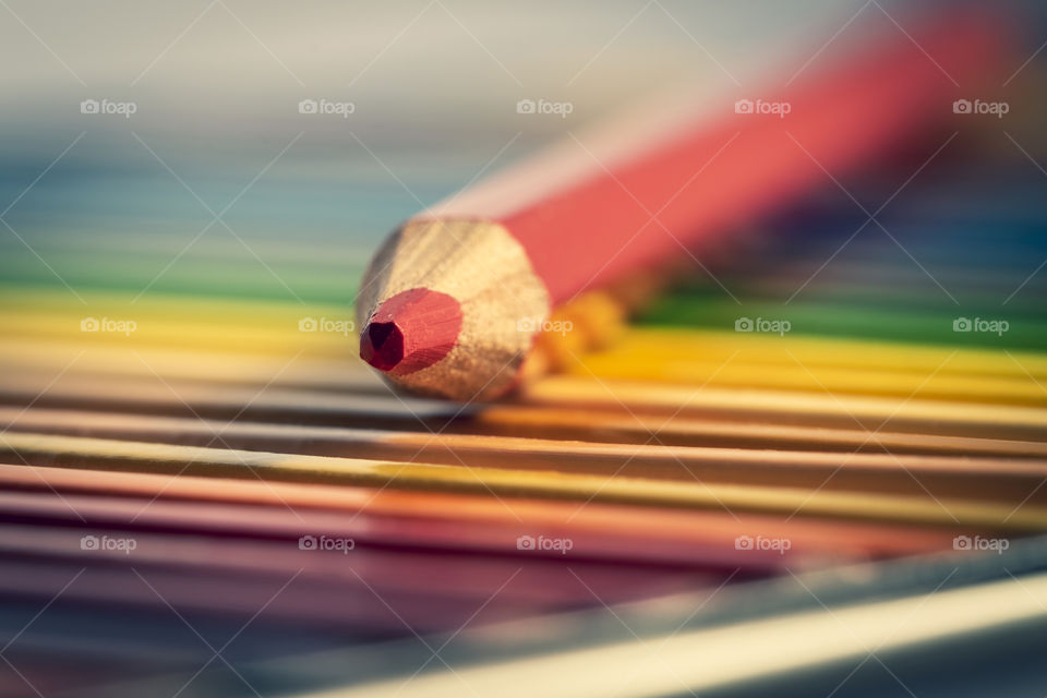 A colorful portrait of a box of pencils to color and create with, with on top of the colors one red colored pencil.