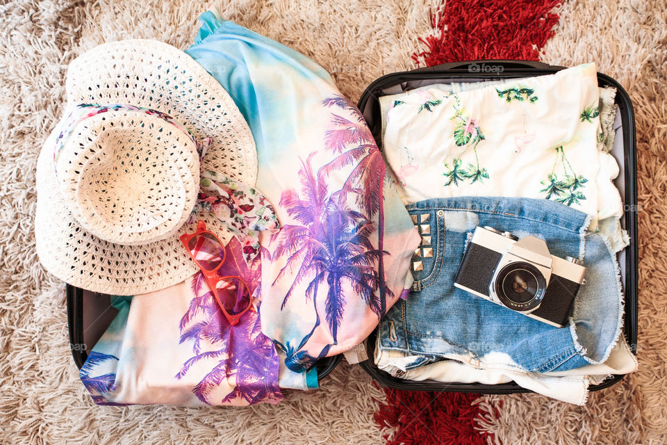 Time for summer vacation. Suitcase with packed summer clothes, a camera, a hat and sunglasses