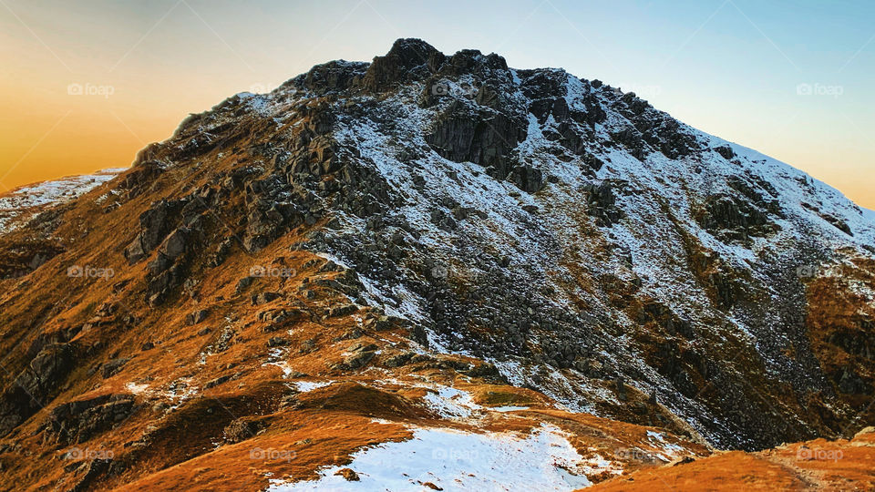 The snowy summit of a beautiful Scottish mountain called Beinn Narnain at sunset, a great hiking and climbing destination for lovers of the great outdoors. 