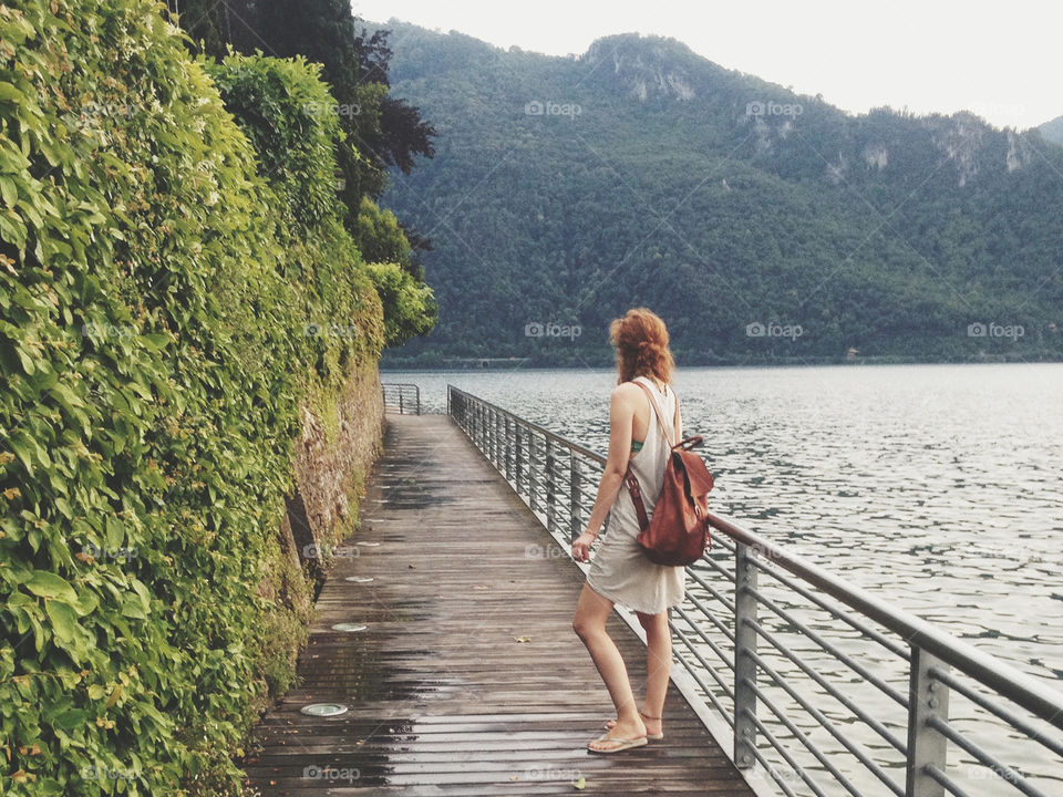 Tall caucasion woman with red hair and backpack on a bridge looking over lake Como in Italy