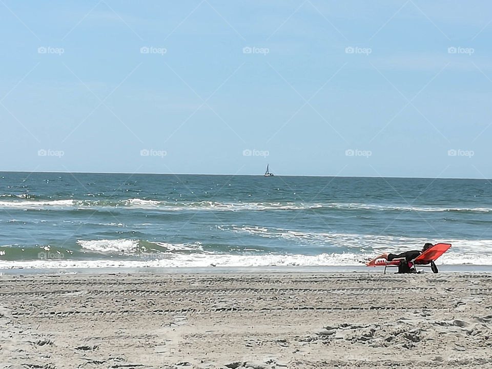 Sunbathing on the beach with sailboat on the horizon