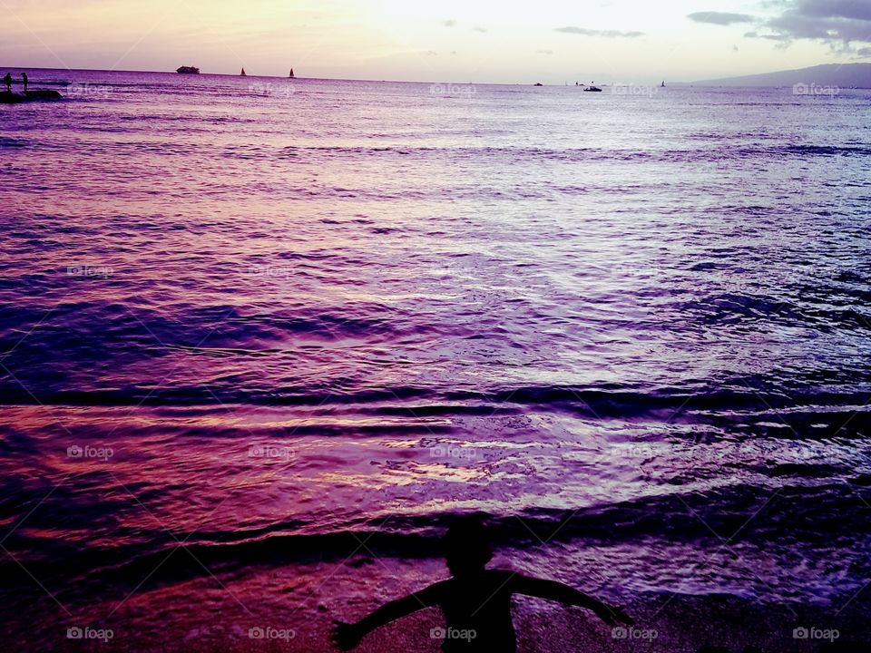 boy poses before the ocean painted purple and pink by the Waikiki Sunset