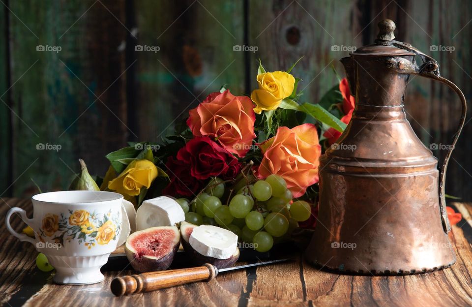 luxurious colorful still life in the style of Dutch artists, goat cheese with grapes and tea and a cup, a bouquet of roses in the background, a copper teapot with tea