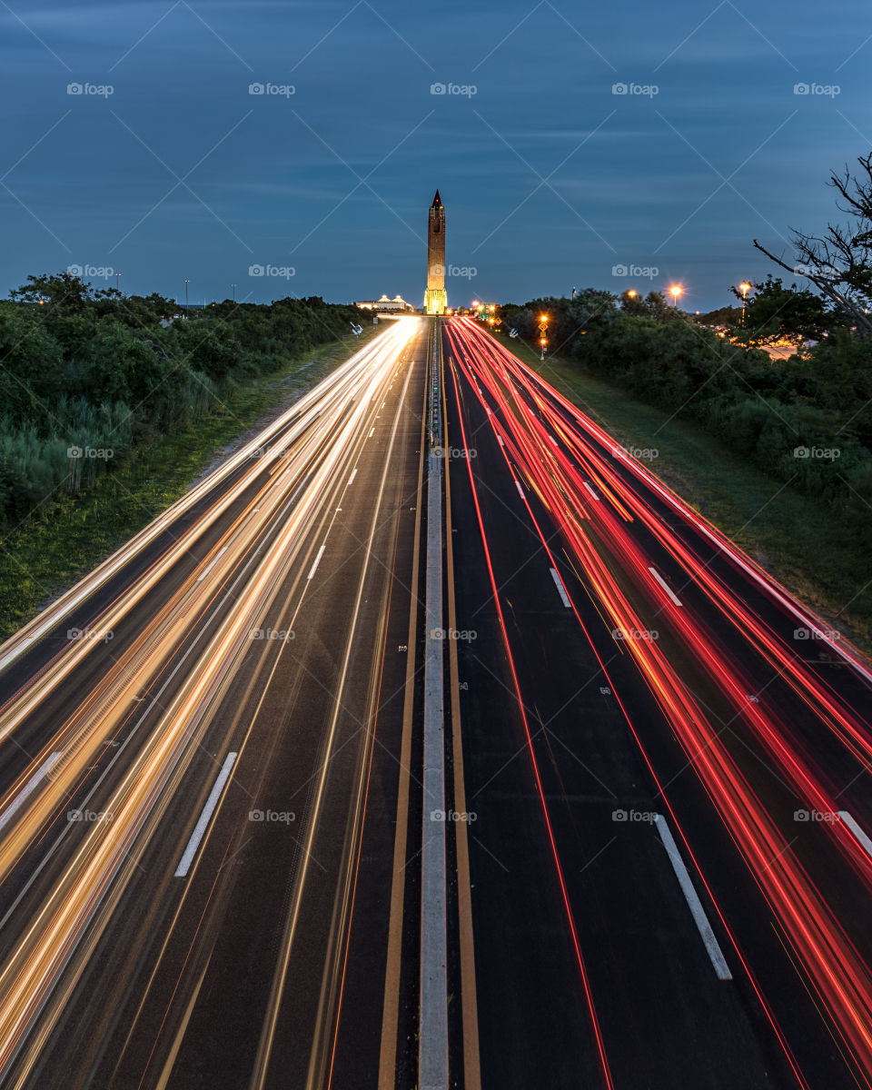 Leading lines of car light trails, streaking down a straight symmetrical highway during rush hour.