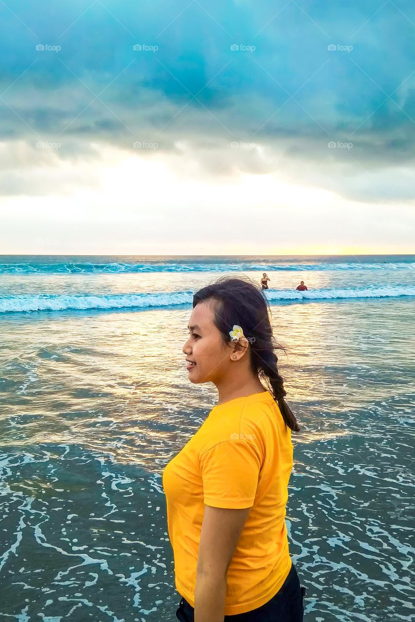 Denpasar, Bali, Indonesia - September 25, 2023: The girl in the yellow dress is standing on the beach in Bali, Indonesia