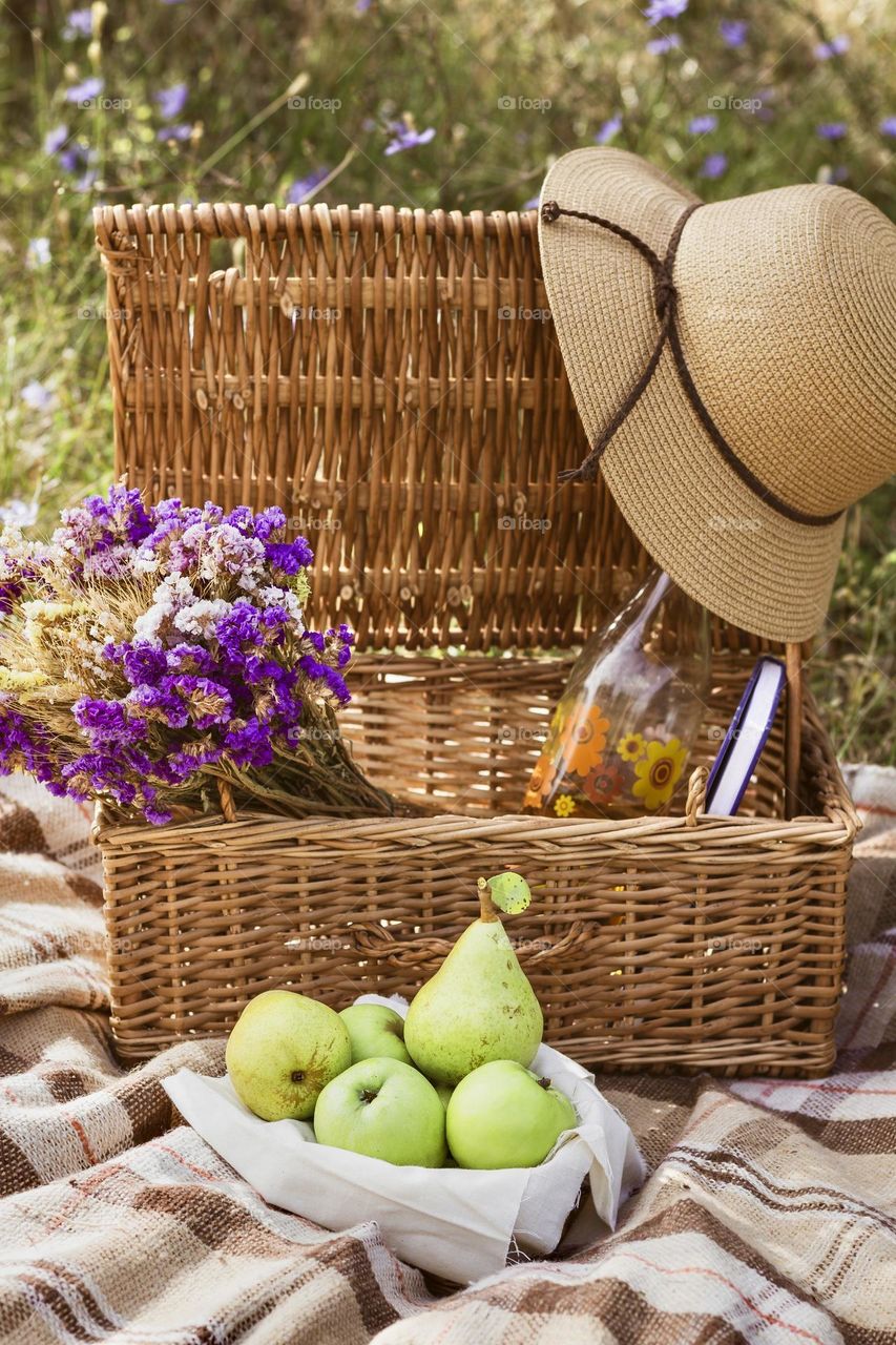 Summer picnic with hamper, bottle, fruit, dried flowers and sun hat.