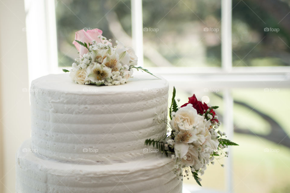White three tier cake with pink and red roses near window