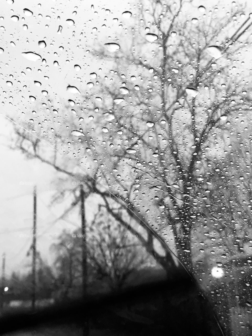 Black and white photo of Looking out side the car window at the rain drops pouring  down from the cloudy gray sky, USA, America 