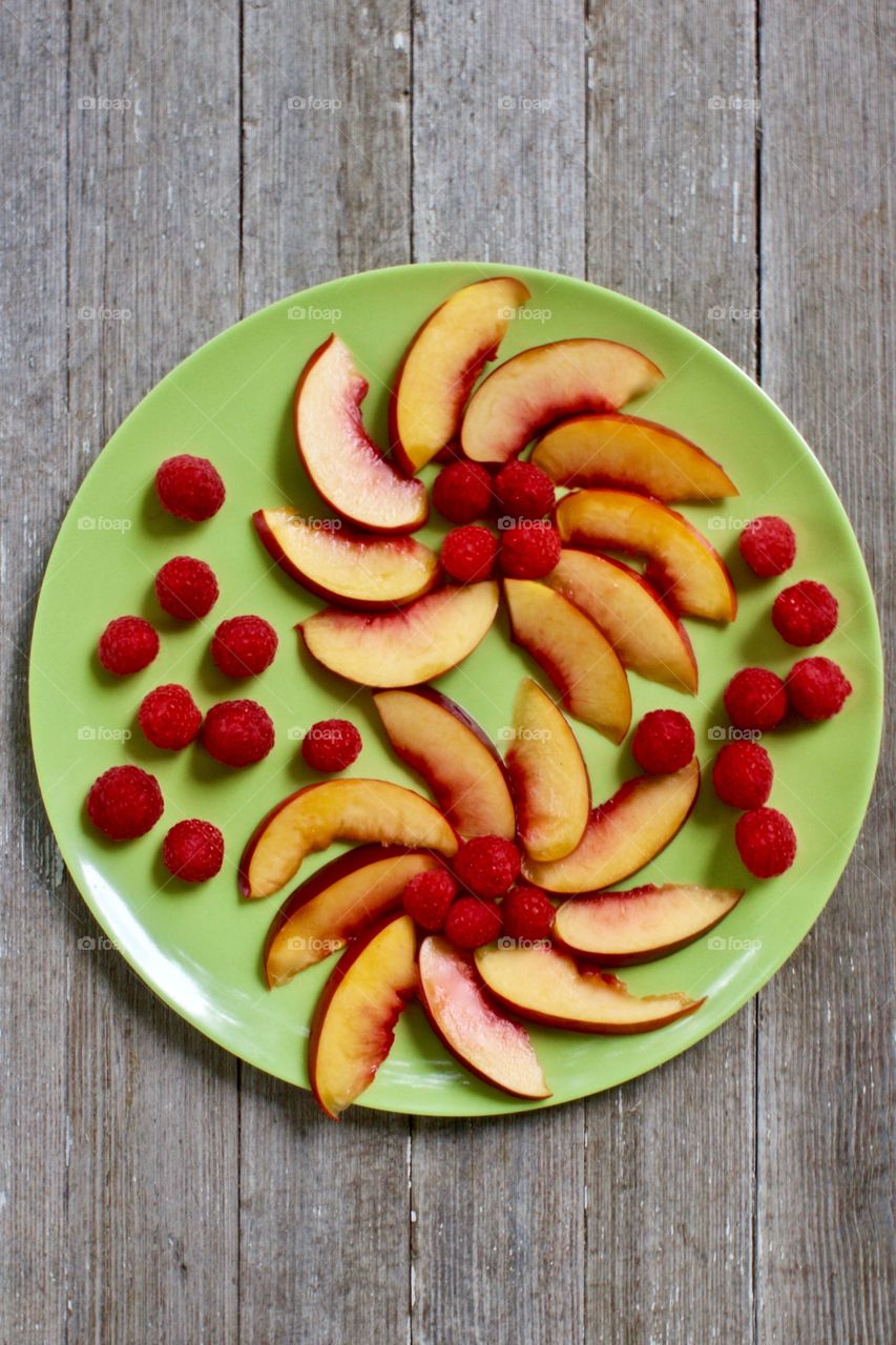 Flat lay of decorative arrangement of fresh nectarine slices and raspberries on a green plate with wooden background 