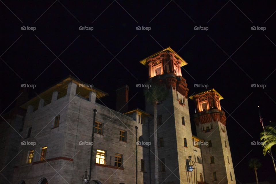 The top of a Spanish-styled building with two towers and a red roof with many windows with lights on against a black night sky