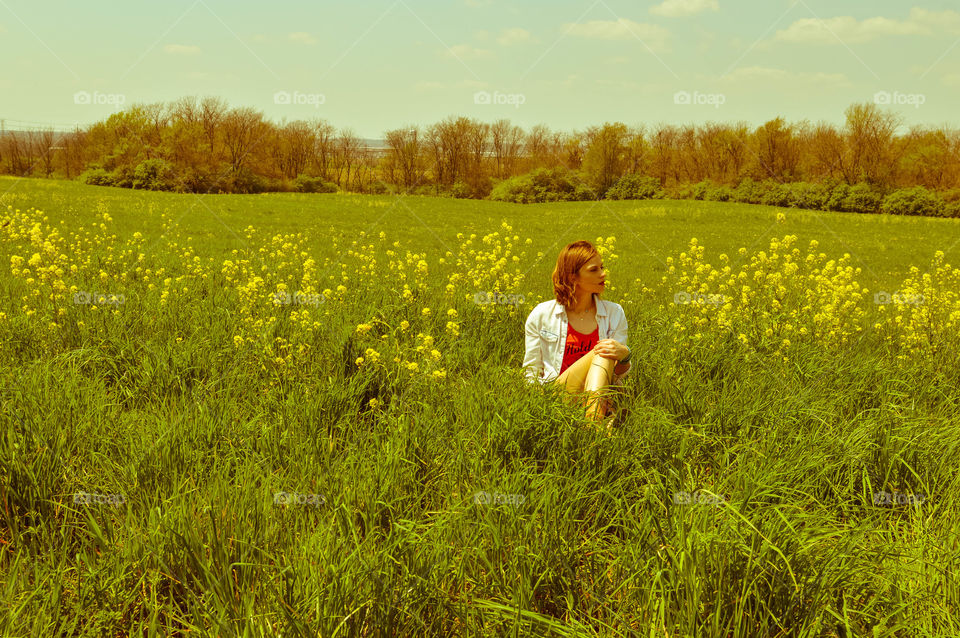 Woman sitting in a field of flowers and looking off in the distance