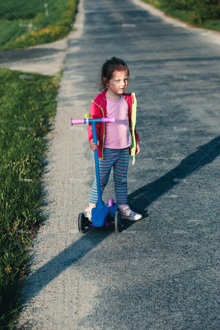 Little adorable girl having fun riding on scooter, playing outdoors. Real people, authentic situations