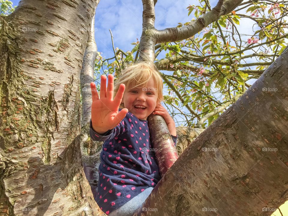 Happy cute girl sitting on tree branch