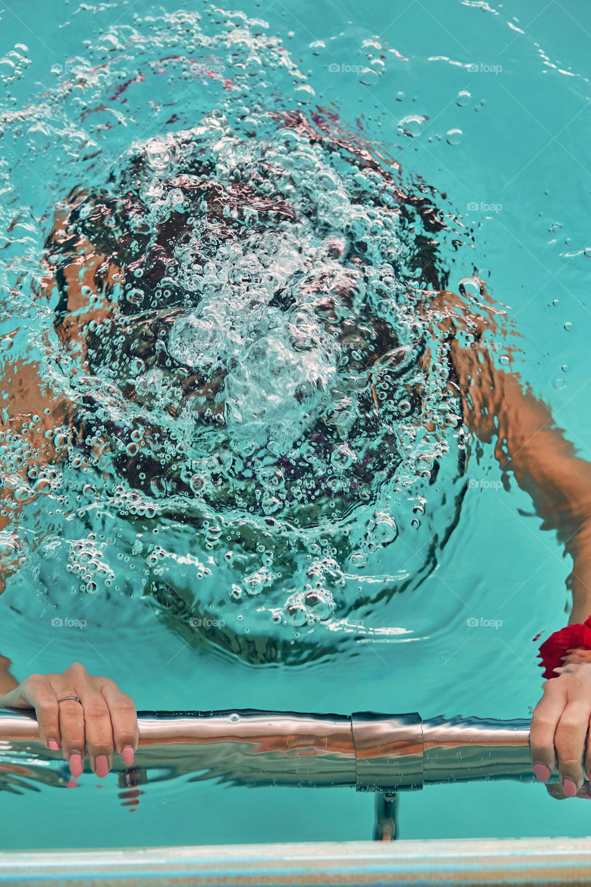 Young woman immersing herself in water, practicing, learning to swim in pool. Candid people, real moments, authentic situations