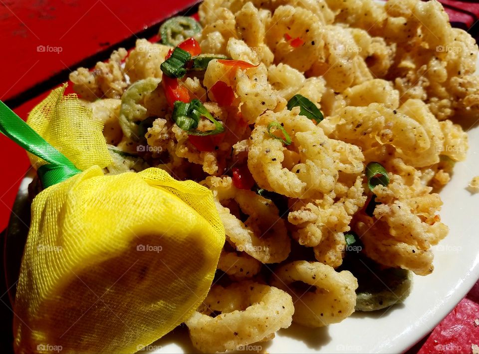 calamari garnished with red and green peppers with a side of lemon and yellow mesh.