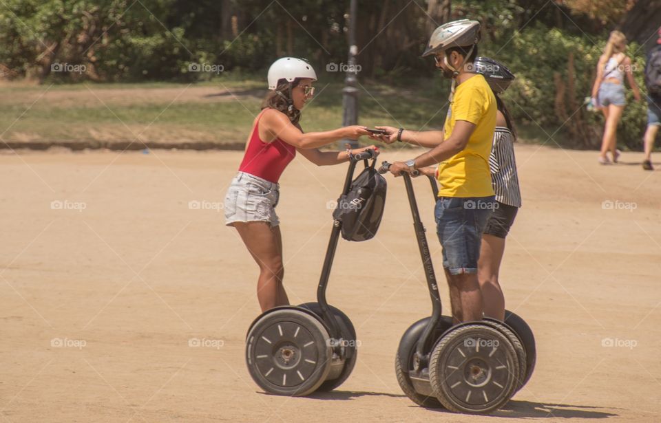 Two tourist rising on a Segway in barcelona to discover the city, one is handing over a mobile phone