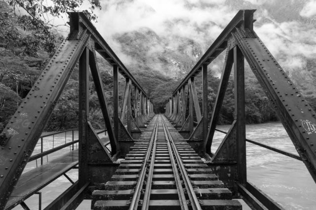Railroad bridge over river. Metal railroad bridge over wide river. Railroad tracks disappear to horizon. Misty mountains in the background